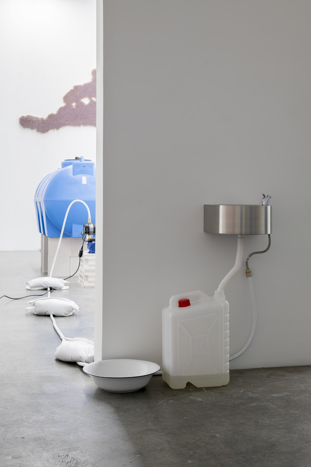 Claire Fontaine La mer à Boire, 2023 1000L blue water tank, pump, automatic pressure controller, 20 mm flexible hydraulic pipe, wall mounted drinking fountain, 80 mm drainage pipes, gerry can, cables, wall mountings and breeze blocks, mains water with 38 grams of salt per litre dimensions variable